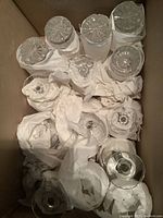 Overhead image showing multiple wrapped glassware items inside a box. Wrapped glasses include some with stemmed bases suggesting snifters or wine glasses.