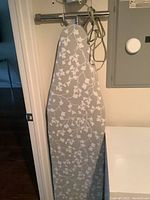 Ironing board with light grey and white floral cover hanging vertically on wall.