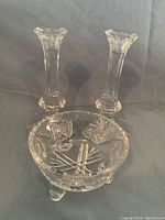 Two clear crystal candlesticks and one round crystal candy dish with pinwheel cut pattern, arranged on gray background.