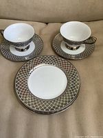 Two porcelain tea cups on saucers with two matching bread plates, showing lattice metallic silver design