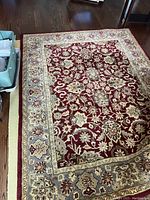 Full view of wool area rug laid out on wooden floor, showing burgundy central panel with floral decorative motifs and surrounding grey and cream borders with intricate designs.