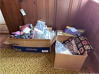 Two boxes filled with assorted afghans, crocheted blankets, woven throws, and textiles in various colors and patterns.