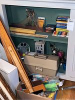 Photo of a shelf containing various art supplies including scissors, rulers, paintbrushes, paint palette, plastic storage box, pipe cleaners, and a wooden box.