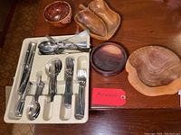 Full view of stainless steel flatware set with spoons, forks, knives, and wood bowls arranged on wooden surface.