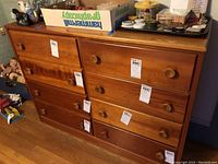 Front view of medium brown wooden dresser with six drawers, some items on top, missing one drawer pull knob visible