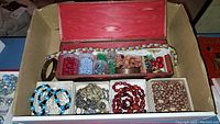 Top view of the wooden box open showing several small containers of beads, floral beaded necklace and some bracelets inside.