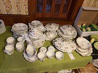 Wide view of porcelain dinnerware and tea service on green tablecloth.