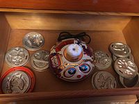 Circular Mattel Makery Bakery electric base with colorful graphics and dials surrounded by multiple shiny metal baking moulds in various shapes including animals and faces.