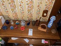Glass paperweights, glass swan and fish, blue and white vase, geode on wooden stand, wooden mortar and pestle, small brown pottery vessel arranged on wooden surface.