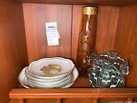 Photo showing 7 decorative plates stacked, tall brown art glass vase, and smaller multi-color ruffled edge vase