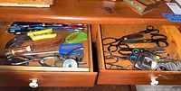 Open drawer showing a variety of scissors, measuring tapes, knife, pens, hole punches, and a stapler