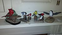 Image showing seven artisan bird sculptures by Kenneth Hovey Taber, including two red cardinals on naturalistic bases, blue jay, yellow finch, and other birds.
