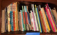Photo showing a variety of colorful vintage children’s books arranged vertically on a wooden shelf, including various Dr. Seuss titles and educational books