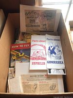 Box containing various vintage printed brochures about syphilis and gonorrhea, Musteroil advertisement, and How to Fly manual.