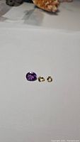 Photo of one purple oval amethyst gemstone and two small golden citrine gemstones on white background.