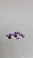 Photo showing a set of 11 natural round amethyst cabochon gemstones with light and medium purple shades on a white background.