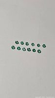 16 natural Zambian calibrated emerald gemstones displayed on white background, showing size and color variety.