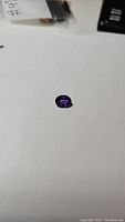 Top view photo of the oval deep purple amethyst gemstone on a white background.