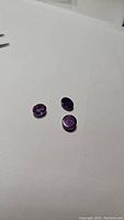 Three purple amethyst cabochon gemstones on a white background showing oval and round cuts with smooth polished surfaces and visible inclusions