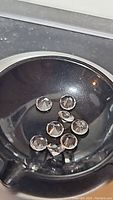 Photo of nine loose diamond-cut clear crystal quartz gemstones in a small black round container viewed from above.