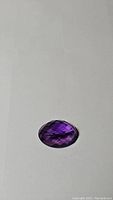 Photo of oval deep purple amethyst with checker cut faceting showing natural inclusions