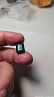 Gemstone held between fingers showing emerald cut and vibrant green color