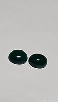 Pair of two deep vivid lime green oval cabochon onyx gemstones on plain surface in ambient light.