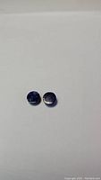 Two small round lapis lazuli gemstones, dark blue, shown on a white background.
