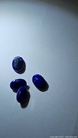 Four deep blue oval lapis lazuli stones viewed from above, showing polished surfaces and some natural pyrite inclusions.