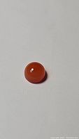 Close-up photo of a single round mandarin orange carnelian cabochon gemstone on white background with good lighting showing its color and polish.