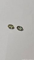 Two oval cut green sillimanite gemstones placed on a white background showing their size and clarity.