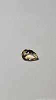 Pear cut natural golden citrine gemstone displayed on white background, showing faceting and color from angled views.