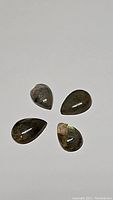 Four pear-shaped natural labradorite cabochons laid out, showing their golden and blue labradorescence flashes under lighting.