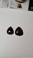Two pear-shaped natural mahogany jasper cabochons with black and reddish-brown pattern on a white background