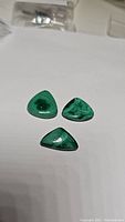 Three triangular natural malachite polished stones with green banded patterns placed on white surface.