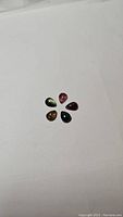 Five pear cabochon cut natural tourmalines of mixed colors including green, pink, red, and brown, arranged in circular pattern on white background.