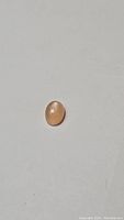 Top view of oval peach moonstone cabochon on white background showing surface and color.