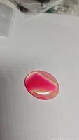 Single vibrant pink oval cabochon with natural agate banding, smooth polished surface, photographed on white background.