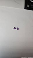 Photo of two small pear tear drop shaped purple amethyst gemstones on white background, showing their color and facets