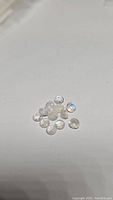 Multiple small round natural rainbow moonstone gemstones with diamond cut facets and blue flash effect laying on white background.