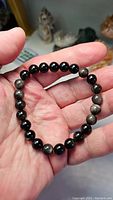 Photo showing silver sheen obsidian bracelet held in hand, displaying black and gray beads with silver flashes.
