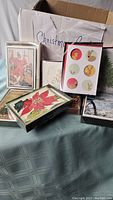 Overview photo showing multiple boxes of Christmas cards with assorted holiday artwork including Santa Claus, poinsettias, reindeer and Christmas tree illustrations; boxes and cards are never used