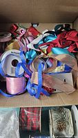 Box with a variety of mixed ribbons including red, blue, and pink ribbons in loose and rolled form