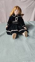 Full view of the porcelain doll seated on a surface, showing navy blue velvet dress and white shoes.