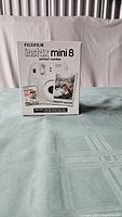 Front view of original FujiFilm Instax Mini 8 box in Dreamy White showing camera image with instant photo example and film pack.