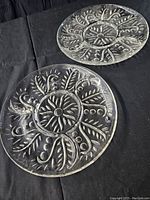 Two clear glass relish trays with embossed floral and leaf pattern, divided into three sections plus center section each.