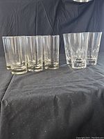 Set of nine highball glasses placed on black cloth, six plain and three with engraved vertical patterns.