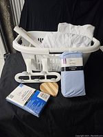 Photo showing all lot contents including the laundry basket, over-the-door hooks, blue King flat sheet, other flat white bedding, and a small wooden accessory.