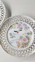 Close-up of one decorative plate showing detailed floral scene with hummingbird and pierced lattice edge.