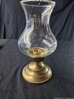 Front view of brass hurricane lamp candle holder with clear glass chimney on dark background.